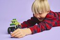 Jongen reikt naar paarse minifiguur bij groene LEGO monster truck.