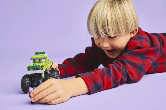 Jongen reikt naar paarse minifiguur bij groene LEGO monster truck.