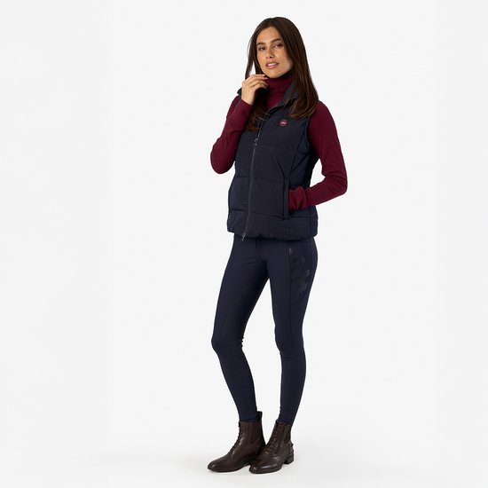 Model draagt een donkerrode coltrui onder een donkerblauw gewatteerd vest en een donkerblauwe rijbroek.