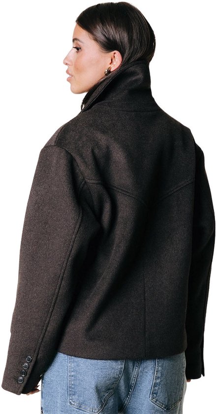 Achterkant van een vrouw die een donkerbruine korte wollen jas met dubbele knopenrij en blauwe jeans draagt.