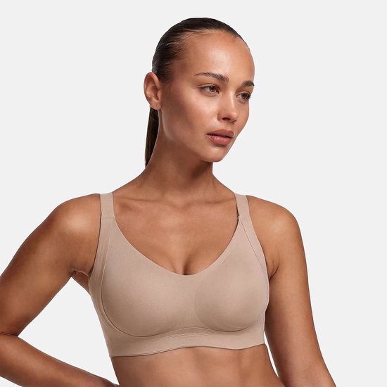 Close-up van model in een beige, naadloze beha met een diepe halslijn en brede bandjes.
