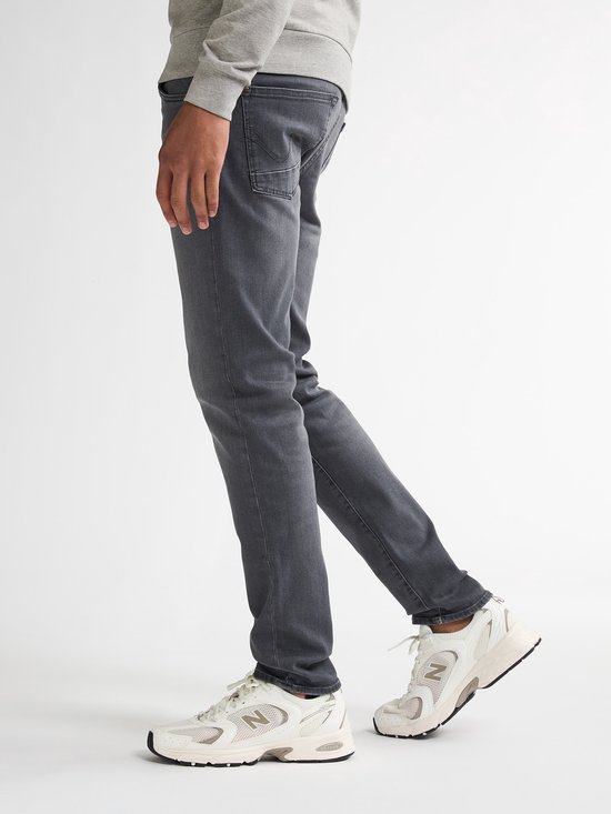 Model draagt een grijze Petrol Industries slim fit jeans en witte New Balance sneakers met beige accenten.