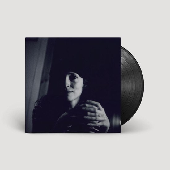 Een zwart vinylalbum met een zwart-wit foto van een vrouw die haar armen om haarzelf slaat.