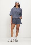 Blauw geknipte casual top met korte mouwen en een V-hals, gedragen door een model met een pet.