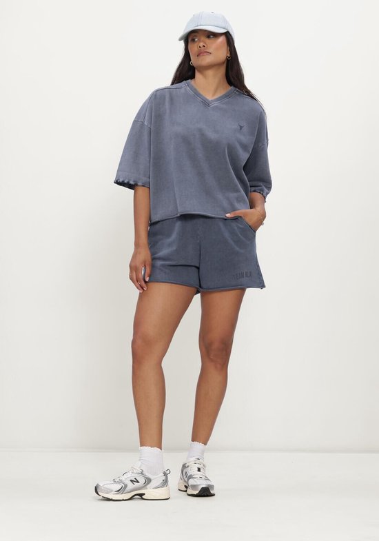 Blauw geknipte casual top met korte mouwen en een V-hals, gedragen door een model met een pet.