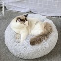 Kortharige kat met witte en bruine vlekken ligt op een ronde, pluizige grijze mand.