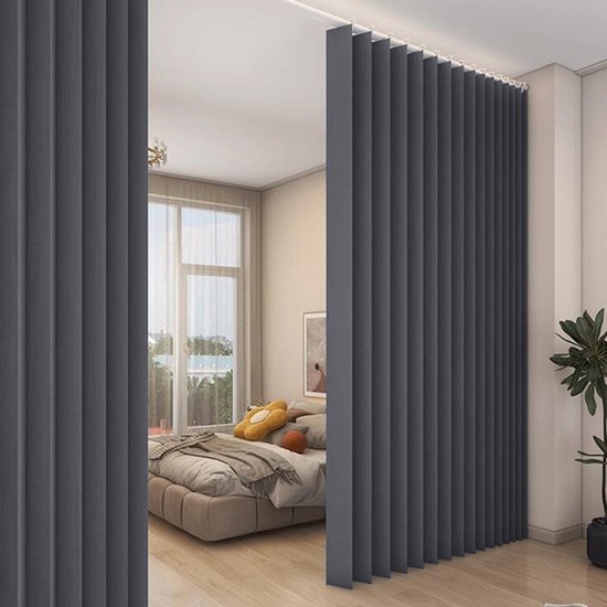 Donkergrijze, geplooide gordijnen verdelen een slaapkamer.