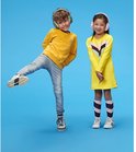 Twee kinderen, een jongen en een meisje, dragen Alpine Muffy gehoorbescherming in verschillende kleuren op een blauwe achtergrond.