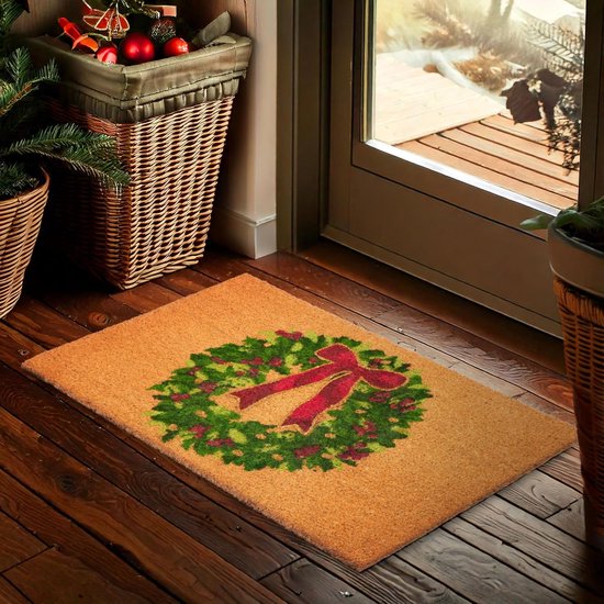 Un paillasson en fibre de coco avec une couronne de Noël et un nœud rouge, placé sur un plancher en bois près d'une porte d'entrée.