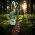 Groene campingtoilet emmer met deksel open en toiletpapier, staand op een bospad.