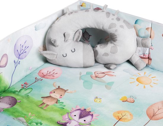 Een giraffe nekkussen in een babygym. De mat heeft afbeeldingen van dieren en bomen, met op de achtergrond een vos op een vliegtuigje.