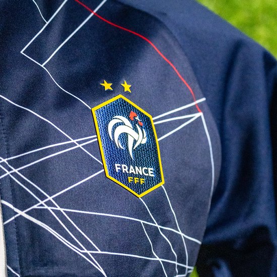 Close-up van het FFF-logo op een donkerblauwe trainingsjas met geometrisch patroon.