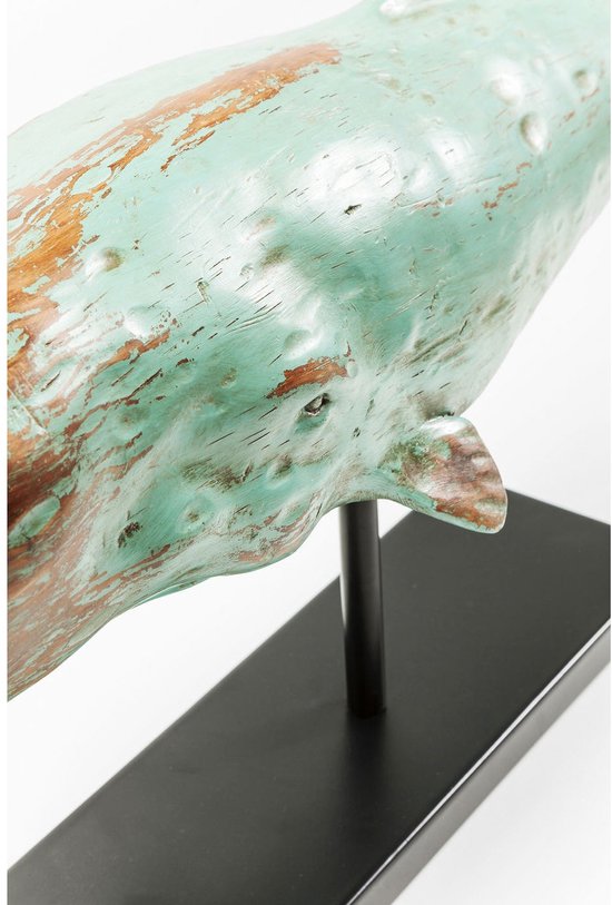 Close-up van een turquoise en bruin verweerd houten walvisbeeld op een zwarte standaard.