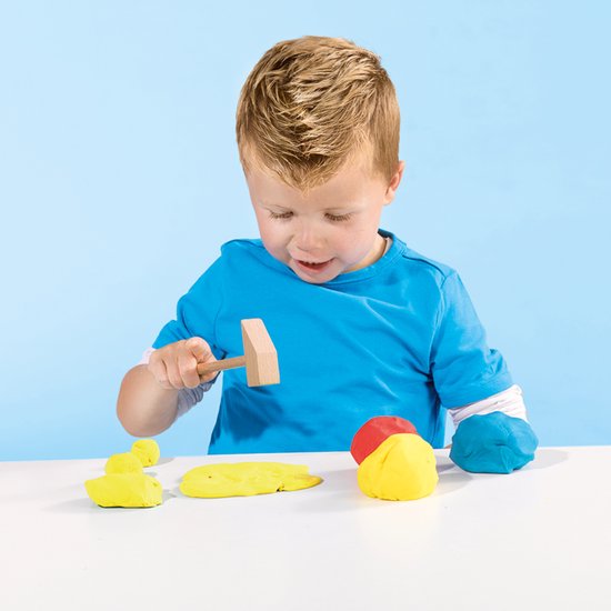 Jongen in blauw shirt speelt met rode, blauwe en gele klei en een houten hamer.