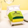 Witte bedvormige sponshouder met gele spons en groen label 'Clean Dreams' naast een wijnglas.