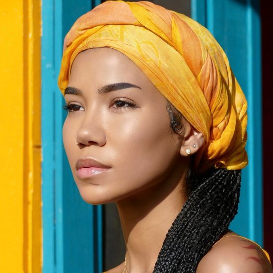 Model met een gele tulband en vlechten, met een blauw-gele achtergrond.