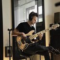 Jonge man met zwarte koptelefoon speelt basgitaar in studio.