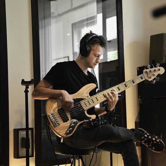 Jonge man met zwarte koptelefoon speelt basgitaar in studio.