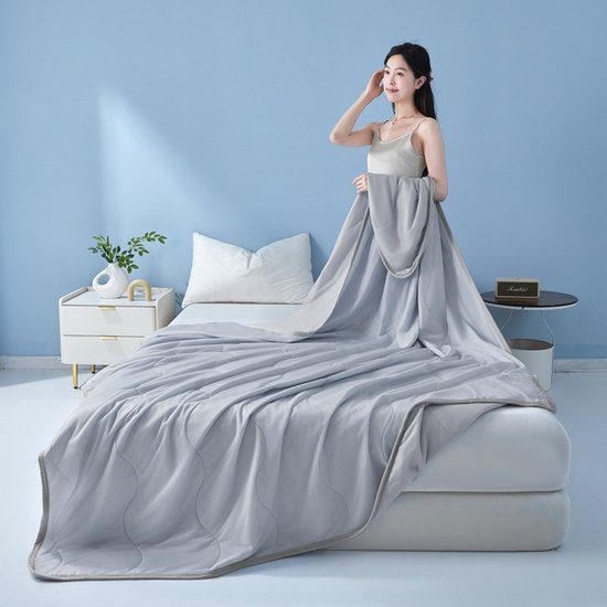 Vrouw op een bed met een lichtgrijs, golvend gewatteerd zomerdeken. 'Enjoy a wonderful night of deep sleep'.