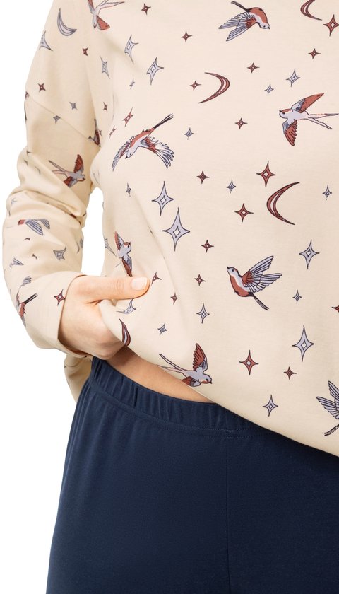 Close-up van een lichtbeige pyjamashirt met lange mouwen, versierd met een print van vogels, manen en sterren.
