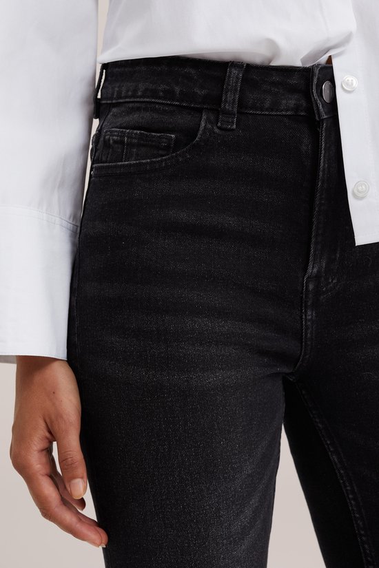Close-up van de tailleband en zakken van een zwarte slim fit jeans.