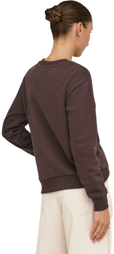 Model draagt bruine sweater met witte hart-applicatie, weggedraaid van de camera.