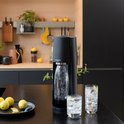 Zwarte SodaStream Terra met glazen fles bruiswater en twee glazen met bruiswater en citroen.