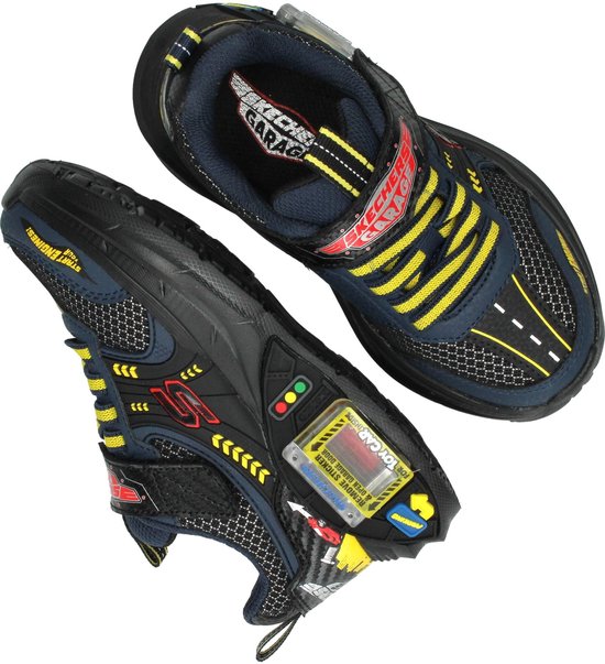 Twee zwarte Skechers veterschoenen met gele en blauwe accenten, raceauto-details en stoplicht-elementen.