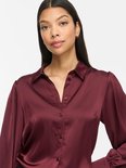 Close-up van model in bordeauxrode satijnen blouse met lange pofmouwen en knoopsluiting.