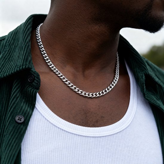Donkere man met een witte tanktop en een groene corduroy jas, draagt een zilverkleurige schakelketting.