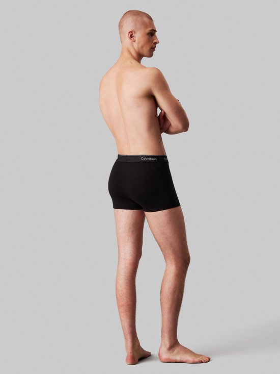 Zij-aanzicht van een model met zwarte Calvin Klein boxerbriefs.
