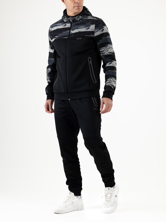 Man met zwart sportjack met camouflageprint op de mouwen en capuchon. Zwarte trainingsbroek en witte sneakers.