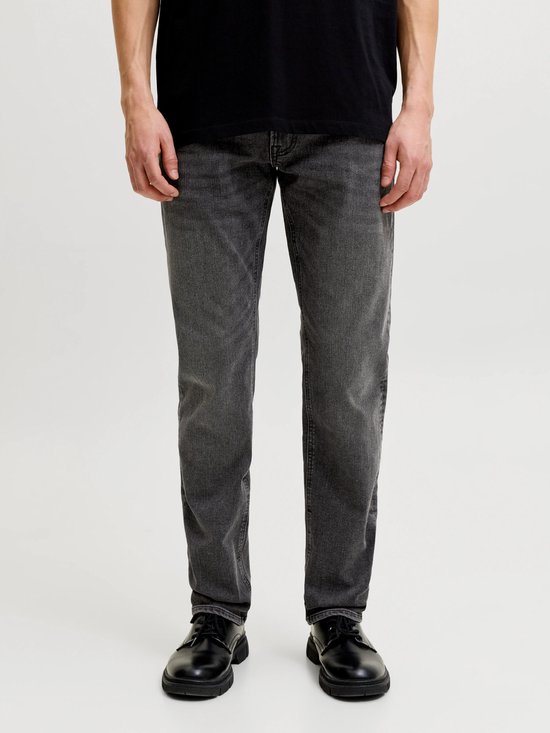 Man in een grijze slim fit jeans met zwarte schoenen en een zwart T-shirt.