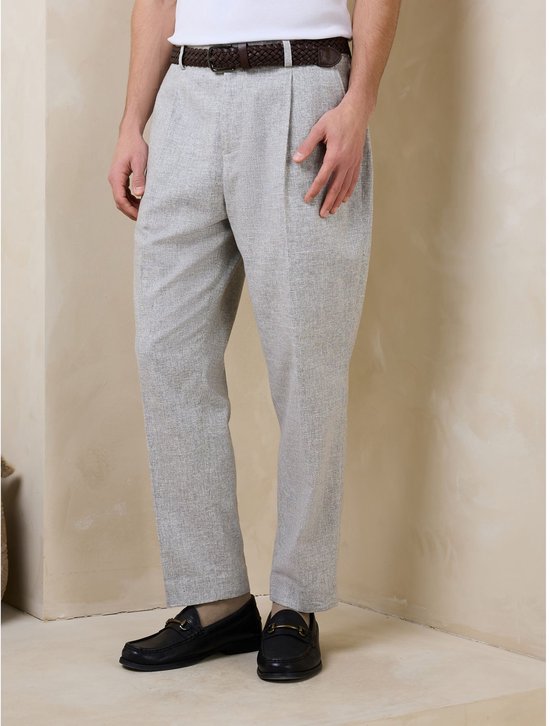 Vooraanzicht van een model dat een grijze pantalon met plooien en een bruine gevlochten riem draagt.