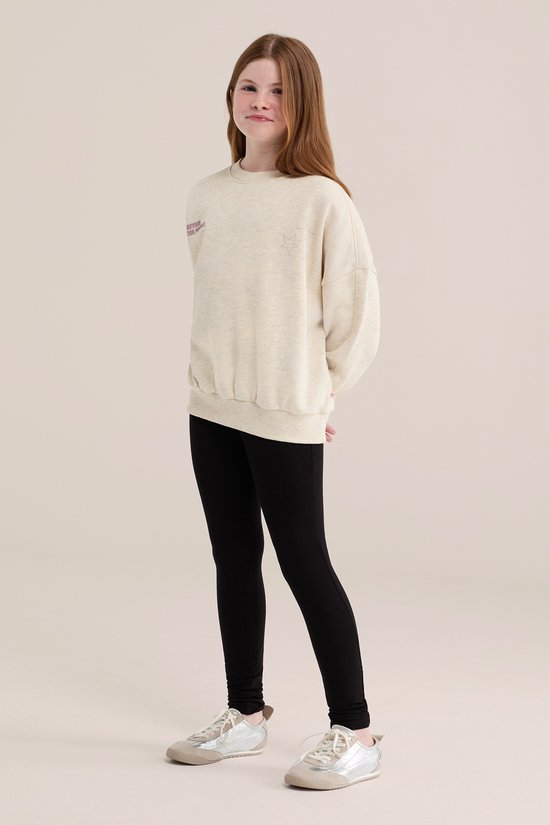 Meisje met lang rood haar, draagt een crèmekleurige sweater met sterprint en zwarte legging.