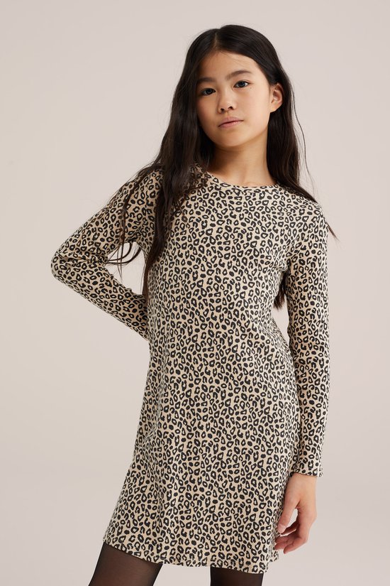 Meisje in een beige jurk met panterprint, met de hand in de zij.