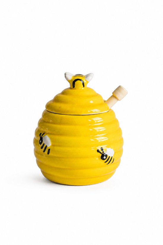 Gele keramische honingpot in bijenhuisvorm met bijendecoratie en houten lepel, geïsoleerd op wit.