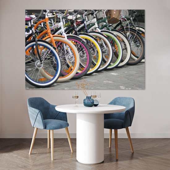 Une rangée de vélos colorés avec des jantes orange, bleues, blanches, roses et jaunes, au-dessus d'une table avec des chaises.