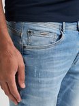 Close-up van de zak van een lichtblauwe jeans, met het 'Petrol' logo.