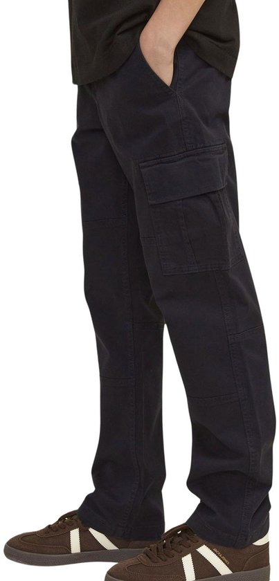 Zijaanzicht van een jongen in donkergrijze cargo broek en bruine sneakers.