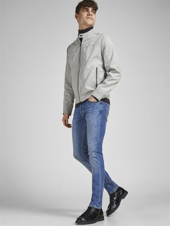Man kijkt naar links, draagt een grijze jas, zwarte coltrui en blauwe jeans.