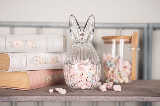 Oeuf de Pâques en verre transparent avec oreilles de lapin, rempli de guimauves roses et pastel.