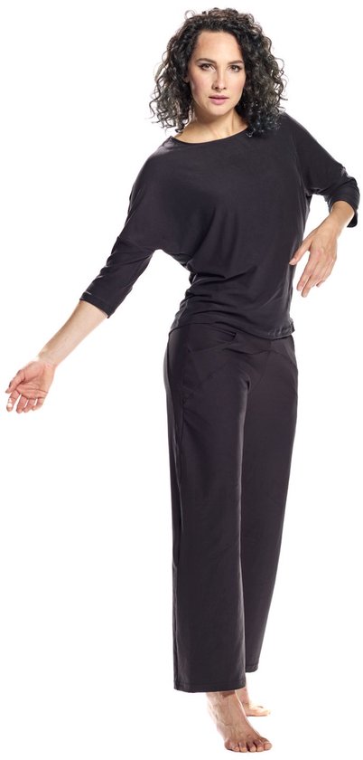 Model draagt een zwarte, wijde driekwartmouw top en zwarte broek met hoge taille. Ze leunt naar voren met een arm uitgestrekt.