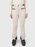Model in beige skibroek met zwarte ritszakken en ski-uitrusting.