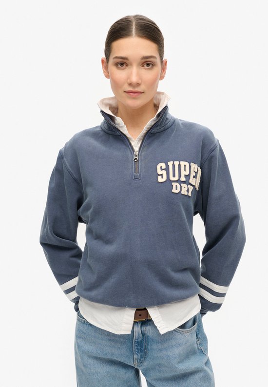 Sweatshirt Superdry bleu-gris avec fermeture éclair partielle, rayures blanches sur les manches et logo Superdry sur la poitrine.