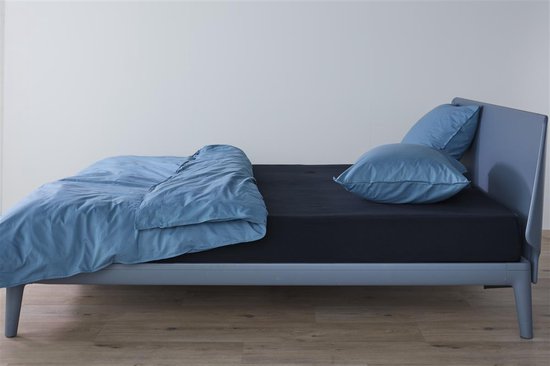 Blauw dekbed en lichtblauwe kussens op een donker hoeslaken op een grijs bed.