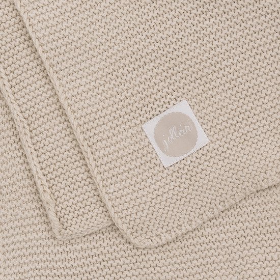 Een beige wiegdeken met een label van Jollein.