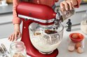 Une femme ajoute des pépites de chocolat à une pâte dans un robot pâtissier KitchenAid Artisan rouge Empire.