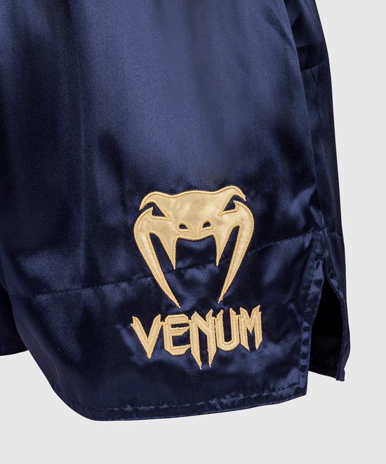Goudkleurig Venum-slanglogo en -woordmerk op de marineblauwe satijnen Muay Thai shorts.