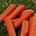 Een stapel oranje Nerf pijltjes met blauwe doppen, liggend op groen gras.